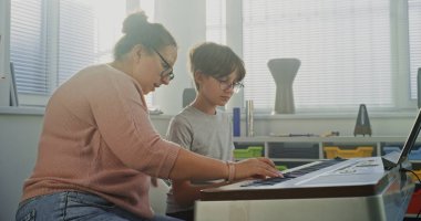 Müzik öğretmeni, ilkokul çocuğuna müzik sınıfında piyano çalması için rehberlik ediyor. Yetenekli Öğrenci Klavye Çalışması, Müzisyen Olmayı Hayal Etme. Müzik Eğitimi, Piyano Eğitimi Dersi, Prova