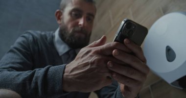 Akıllı Telefon Kullanan İşadamı, Tuvalette Oturan. Man Scrolling Social Networks ve Media Content, Modern Office 'in tuvaletinde rahatlamak. Yaşam tarzı ve günlük rutin. Kapat..