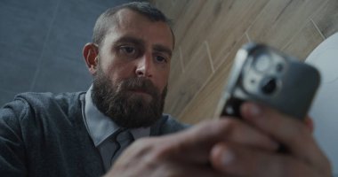 Erkek Ofis İşçisinin Kapanışı Tuvalette Oturan ve Akıllı Telefonu Kaydıran. İş Adamı Sosyal Ağ ve Medya İçeriğinde Sörf Yapıyor, Çalışırken Tuvalette Rahat Hissediyor. Günlük rutin ve yaşam tarzı.