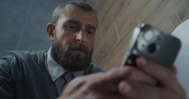 Erkek Ofis İşçisinin Kapanışı Tuvalette Oturan ve Akıllı Telefonu Kaydıran. İş Adamı Sosyal Ağ ve Medya İçeriğinde Sörf Yapıyor, Çalışırken Tuvalette Rahat Hissediyor. Günlük rutin ve yaşam tarzı.