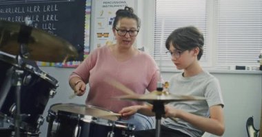 İlkokulda perküsyon dersi sırasında davul çalan yetenekli çocuk, ritim duygusunu geliştiriyor. Genç Müzisyen Öğretmeni Müzik Dersinde Davul Çalmayı Öğretmek. Müzik Enstrümanları Çalışması.