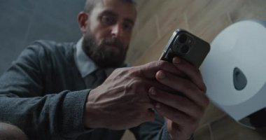 Akıllı Telefon Kullanan İşadamı, Tuvalette Oturan. Man Scrolling Social Networks ve Media Content, Modern Office 'in tuvaletinde rahatlamak. Yaşam tarzı ve günlük rutin. Kapat..