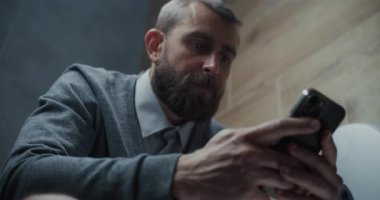 Tuvalette oturan ve akıllı telefonları kaydıran erkek ofis çalışanı. İş Adamı Sosyal Ağ ve Medya İçeriğinde Sörf Yapıyor, Çalışırken Tuvalette Rahat Hissediyor. Günlük rutin ve yaşam tarzı. Düşük Açı.