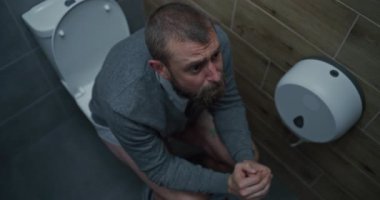 İshal ve hazımsızlık çeken ve tuvalette oturan gergin yüz ifadesi olan bir iş adamı. Adamın Karnı Karışık, Ofis Tuvaletinde Sindirim Rahatsızlığı. Yüksek Açı