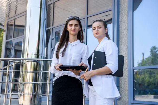 Two business women with tablets standing outside business building