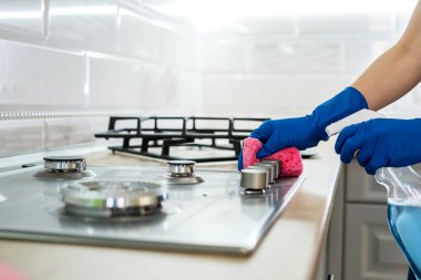 Mutfakta lastik eldivenlerle paslanmaz çelik gaz yüzeyi temizleyen kadın..