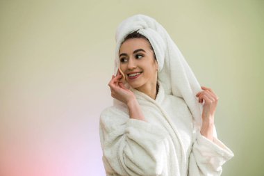 Duş aldıktan sonra bornoz ve havlu giyen güzel genç bir kadın makyaj yapıyor. Yüzüne pudra sür..