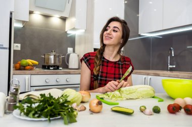 Mutfak masasında poz veren kız sağlıklı bir yaşam için farklı sebze ve sebzelerden oluşan bir salata hazırlıyor.