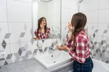 Güzel bir kadın banyo yaptıktan sonra yüzüne nemlendirici krem sürüyor. Cilt bakımı