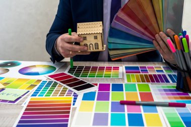 Takım elbiseli genç tasarımcı iş yerindeki kumaş örneği veya katalog palet rehberinden renk seçiyor. Tabloda boya rengi palet örnekleri olan grafik tasarımcısı, kapat