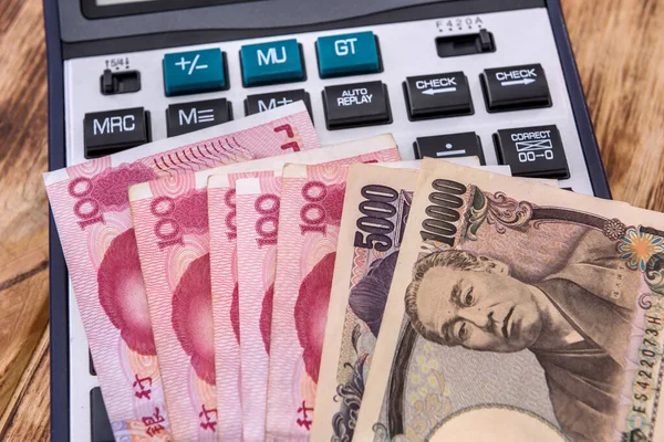 Tahta arka planda Çince ve Japon banknotları olan hesap makinesi. Yakın plan.