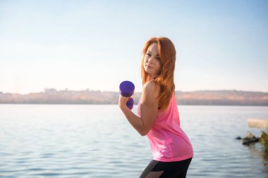 Spor salonundaki kadın gölün küçük ağırlıklarıyla sabah egzersizi yapıyor.