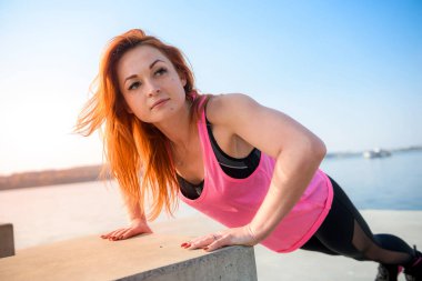 Genç sporcu kadın göl kenarında şınav çekiyor. Spor ve eğitim kavramları.