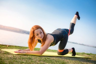 Güzel genç bir kadın sabah parkta çalışmadan önce esneme egzersizi yapıyor.