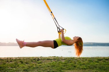Genç bayan sporcu parkta trx fitness kayışlarıyla antrenman yapıyor. Sağlıklı çalışma ve yaşam tarzı kavramı