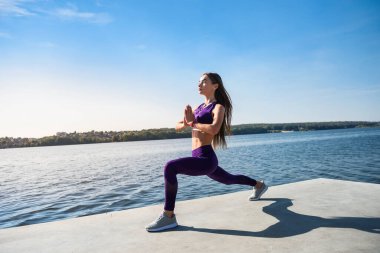 Spor yapan kadın gündüz vakti gölün yanındaki parkta yoga egzersizi yapıyor. Sağlıklı yaşam tarzı kavramı