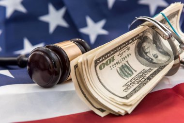Metal kelepçeler, hakimin çekici ve Amerikan bayrağında duran dolar banknotları. Mali suçlar veya yolsuzluk kavramı