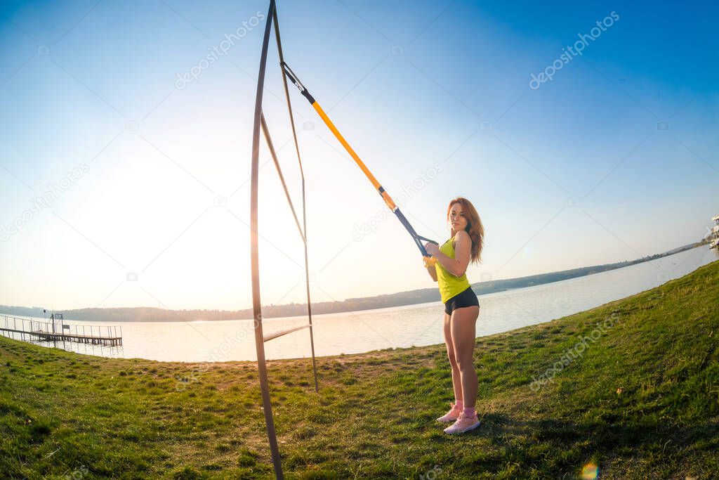 sport woman doing  training outdoors with TRX at daytime. Total body resistance exercises for her healhty lifestyle.