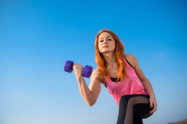 Fitness egzersizi. Spor salonunda dambıl kullanan genç bir kadın dışarıda egzersiz yapıyor. Sağlıklı yaşam tarzı.