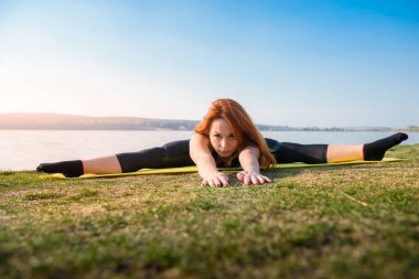 Spor kıyafetleri içinde genç ve çekici bir kadın gündüz vakti çimlerin üzerinde ısınma sicimi geriyor. Sağlıklı yaşam tarzı