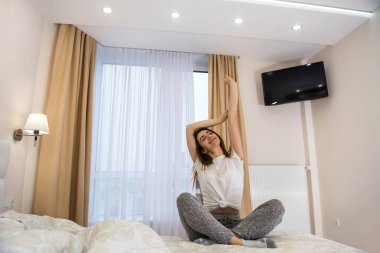 Yatakta oturan güzel genç kız yoga ya da sabah egzersizi yapıyor. Güzellik ve sağlıklı yaşam tarzı kavramı.