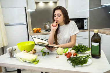 Genç bir kadın mutfakta not defterini kullanarak yemek pişiriyor. .