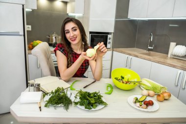 Mutfak masasında poz veren kız sağlıklı bir yaşam için farklı sebze ve sebzelerden oluşan bir salata hazırlıyor.