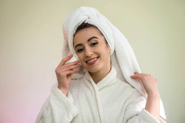 beautiful young woman in a bathrobe and towel after shower  is doing herself a makeover -  apply powder on face.