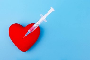 Kırmızı kalp ve mavi arka planda bir şırınga.