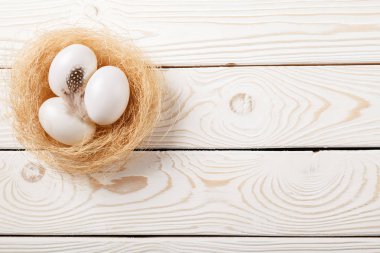 Paskalya arka plan. Beyaz yumurta ve tüy yuvaya rustik beyaz ahşap zemin üzerinde. Üstten görünüm, kopya alanı