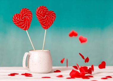 Sevgililer günü arka plan. Mavi bir arka plan üzerinde beyaz bir fincan ve tablo beyaz zemin üzerine düşen küçük kalpler kalp şeklinde iki lolipop. Sevgililer günü veya düğün günü için kavram