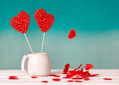 Sevgililer günü arka plan. Mavi bir arka plan üzerinde beyaz bir fincan ve tablo beyaz zemin üzerine düşen küçük kalpler kalp şeklinde iki lolipop. Sevgililer günü veya düğün günü için kavram