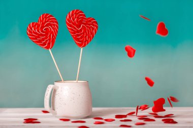 Sevgililer günü arka plan. Mavi bir arka plan üzerinde beyaz bir fincan ve tablo beyaz zemin üzerine düşen küçük kalpler kalp şeklinde iki lolipop. Sevgililer günü veya düğün günü için kavram
