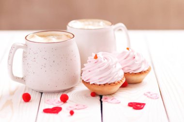İki bardak kahve ve Sevgililer günü veya Doğum günü, düğün günü için pembe krema ile cupcakes. Beyaz ahşap arka plan. Seçici odak