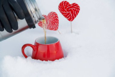 Sevgililer günü pikniğe üzerinde temiz havada bir termos çaydan dökme. Soğuk gün sahilde. Sıcak çay ve sıcak buhar, karda lolipop kalpleri ile kırmızı kupalar. Romantik arka plan