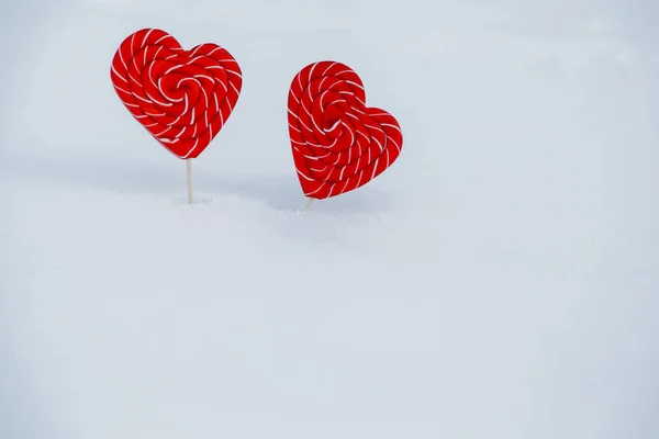 two hearts-candy in the snow. concept of Declaration of love and sweets, Valentine\'s day. heart Lollipop, sweet symbol of love. Valentines heart made of sugar on snow background. close up, soft focus
