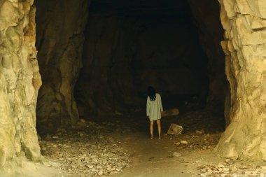 Uzun bir t-shirt ve pembe ayakkabılarla bir kadında yüksek taş zemin üzerine büyük bir taş üzerinde duruyor. Kadın mağaraya girişinde önünde durdu