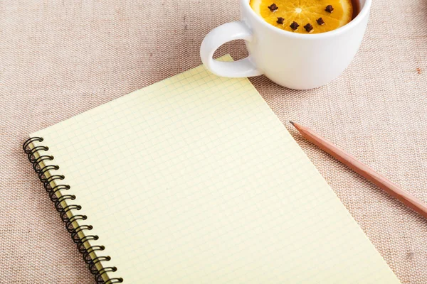 A Cup of tea with a piece of orange and cloves next to a pencil and a notebook on a table covered with a linen tablecloth, write down the list of actions. Concept of planning. Top view, copy space