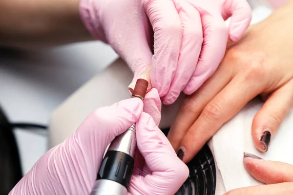 Closeup shot of hardware manicure in a beauty salon. Manicure process, cleaning of nails by a milling cutter. Procedure for the preparation of nails before applying nail polish.