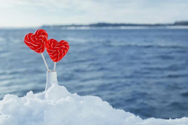 Valentine\'s day background. Candy hearts in a vase in the snow against the sea or river. Romantic date and Declaration of love on the frosty snowy shore