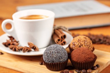 Kahve molası bir fincan sıcak kahve ve kek üzerinde açık bir kitap ile ahşap bir masa. Beyaz fincan siyah kahve kavrulmuş kahve çekirdekleri, tarçın ve anason az miktarda tarafından çevrili