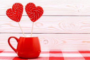 Sevgililer günü arka plan. İki kalp lolipop Beyaz ahşap zemin üzerinde kareli bir masa örtüsü üzerinde kırmızı bir fincan şeklinde. Tebrik kartı.
