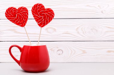 Beyaz ahşap zemin üzerinde Sevgililer günü için kırmızı Kupası, lolipop kalp şeklinde. Tebrik kartı