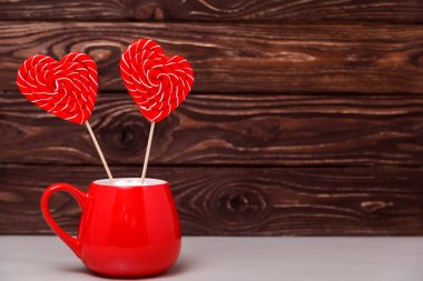 Kalp lolipop ahşap arka plan üzerinde kırmızı Sevgililer günü kupa şeklinde. Tebrik kartı