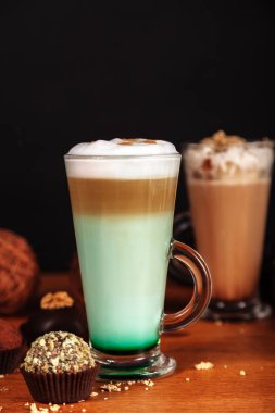 Kahve latte macchiato nane şurubu ve krema kek ile karanlık bir arka plan üzerinde ahşap bir masa üzerinde yüksek şeffaf gözlük