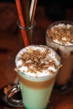 Kahve latte macchiato nane şurubu ve krem şanti ile serpilir ile kıyılmış helva, ahşap bir masa üzerinde yüksek şeffaf gözlük