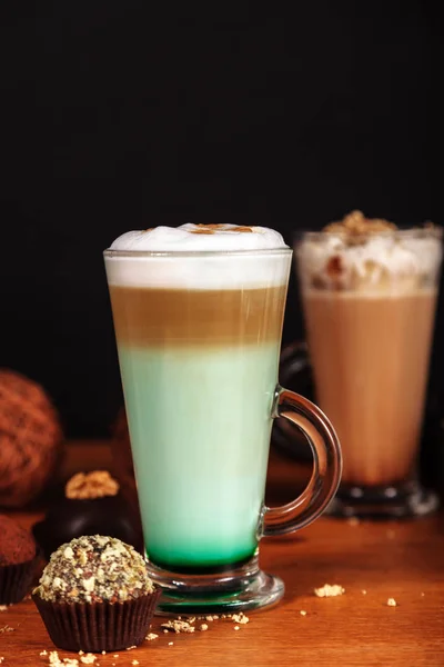 Kahve latte macchiato nane şurubu ve krema kek ile karanlık bir arka plan üzerinde ahşap bir masa üzerinde yüksek şeffaf gözlük