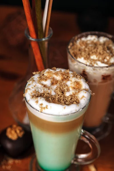 Coffee latte macchiato with mint syrup and whipped cream, sprinkled with chopped halva, in high transparent glasses, on a wooden table