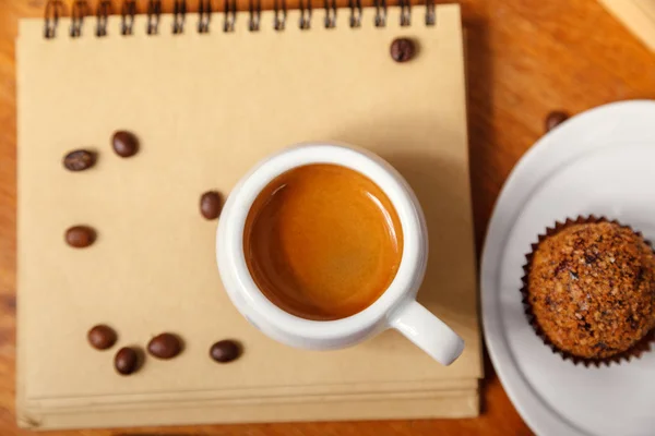 Bir fincan espresso köpük ve bir defter ile ahşap bir masa kahve çekirdekleri dağınık. Kahve molası kavramı