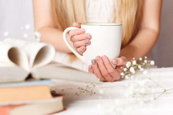 A Cup of tea in women's hands. Cozy concept for spring morning. Spring flower tea in a white Cup on the table with books and flowers.